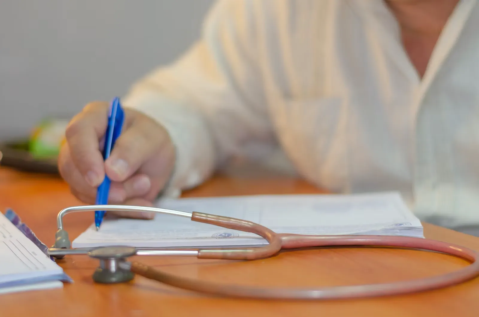 A person writing on a sheet of paper next to a stethoscope, the paperwork stage of medical registration in India