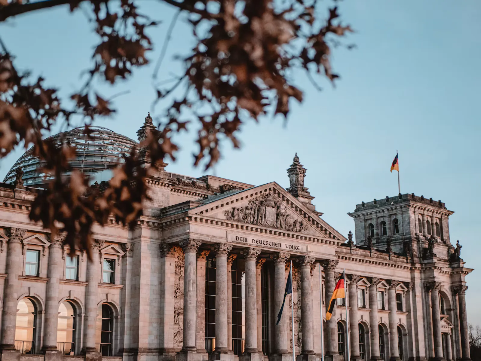 Reichstagsgebäude in Berlin im Abendlicht mit Glaskuppel, Inschrift Dem deutschen Volke und Deutschlandflagge, im Vordergrund unscharfe Herbstblätter