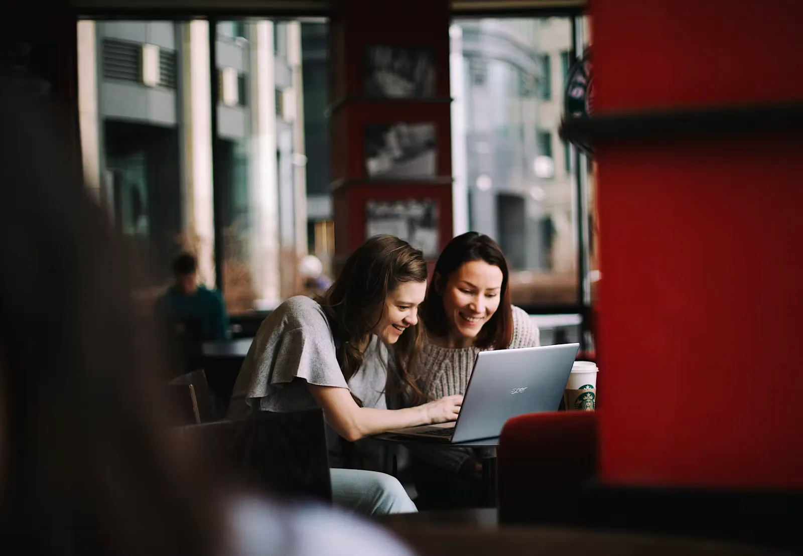 Zwei Studentinnen sitzen in einem Café und schauen gemeinsam auf einen Laptop