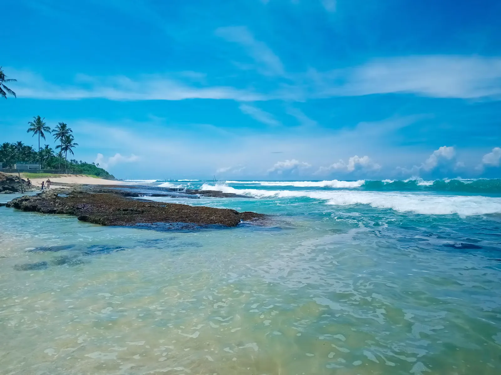 Grüne Bäume auf einer Felsformation am Meer unter blauem Himmel