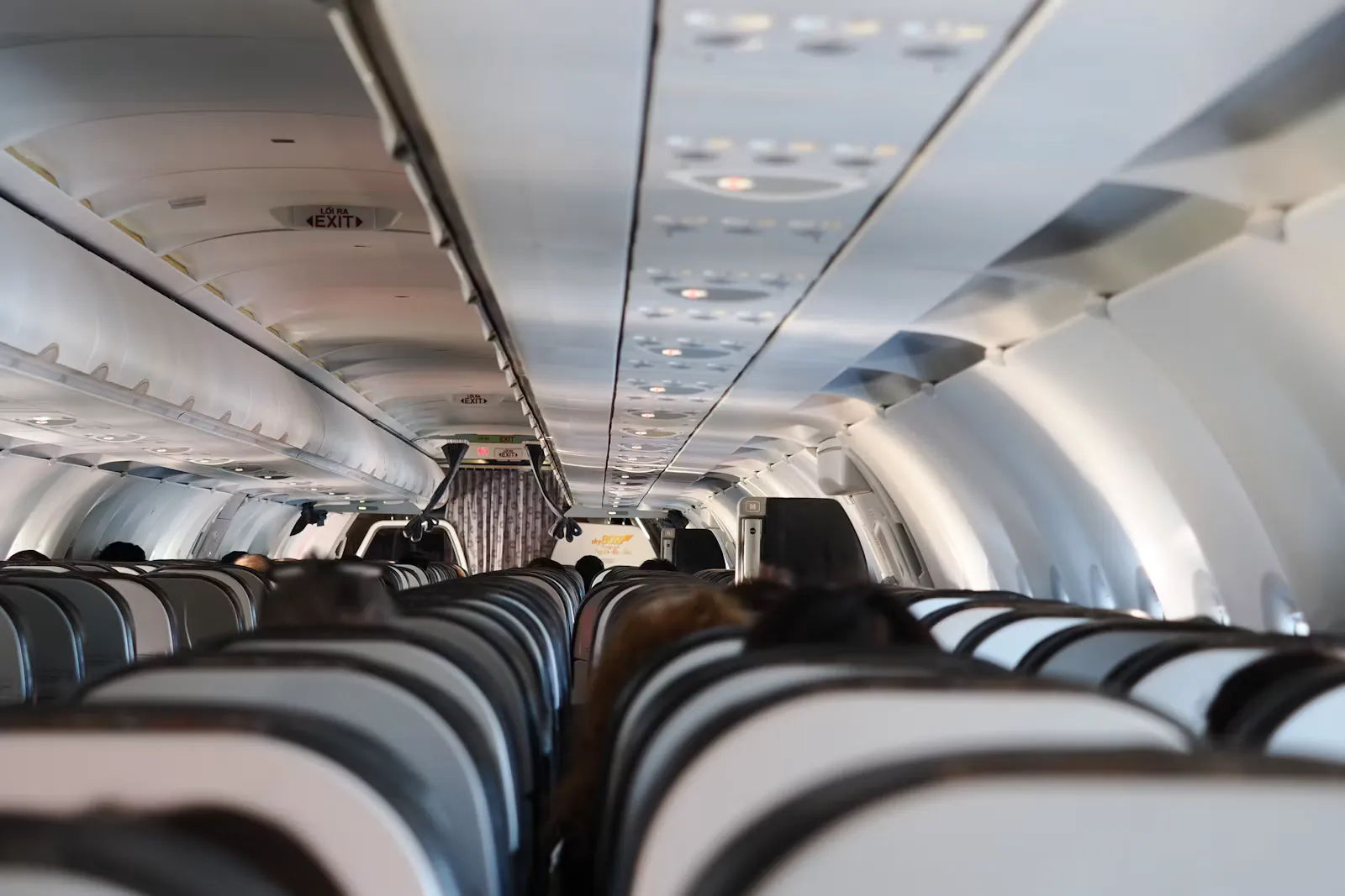 Kabine eines Passagierflugzeugs mit vollen Sitzreihen und geschlossenen Gepäckfächern, Blick durch den Mittelgang Richtung Notausgang