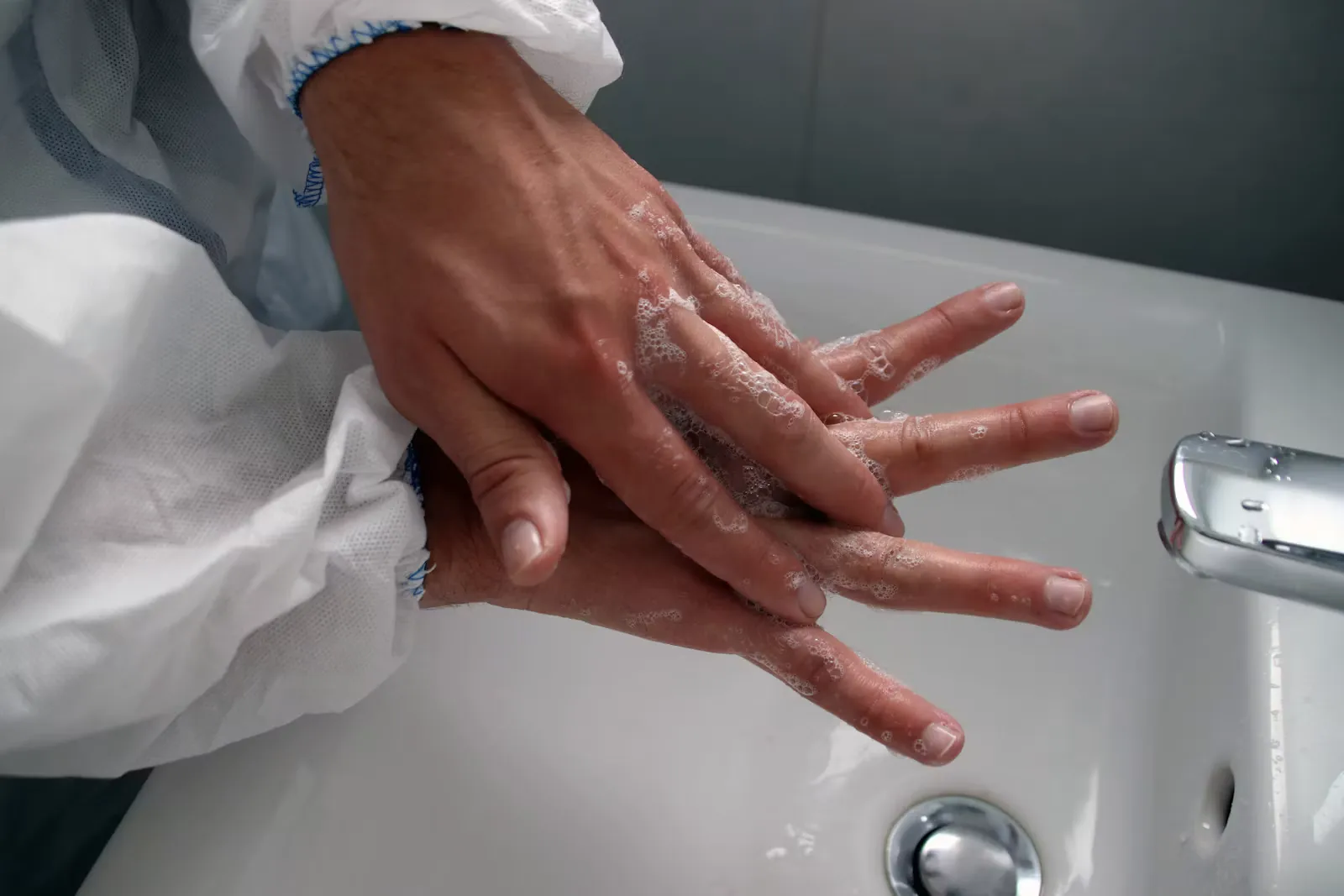 A close-up of a person's hand held under a running tap over a white ceramic sink