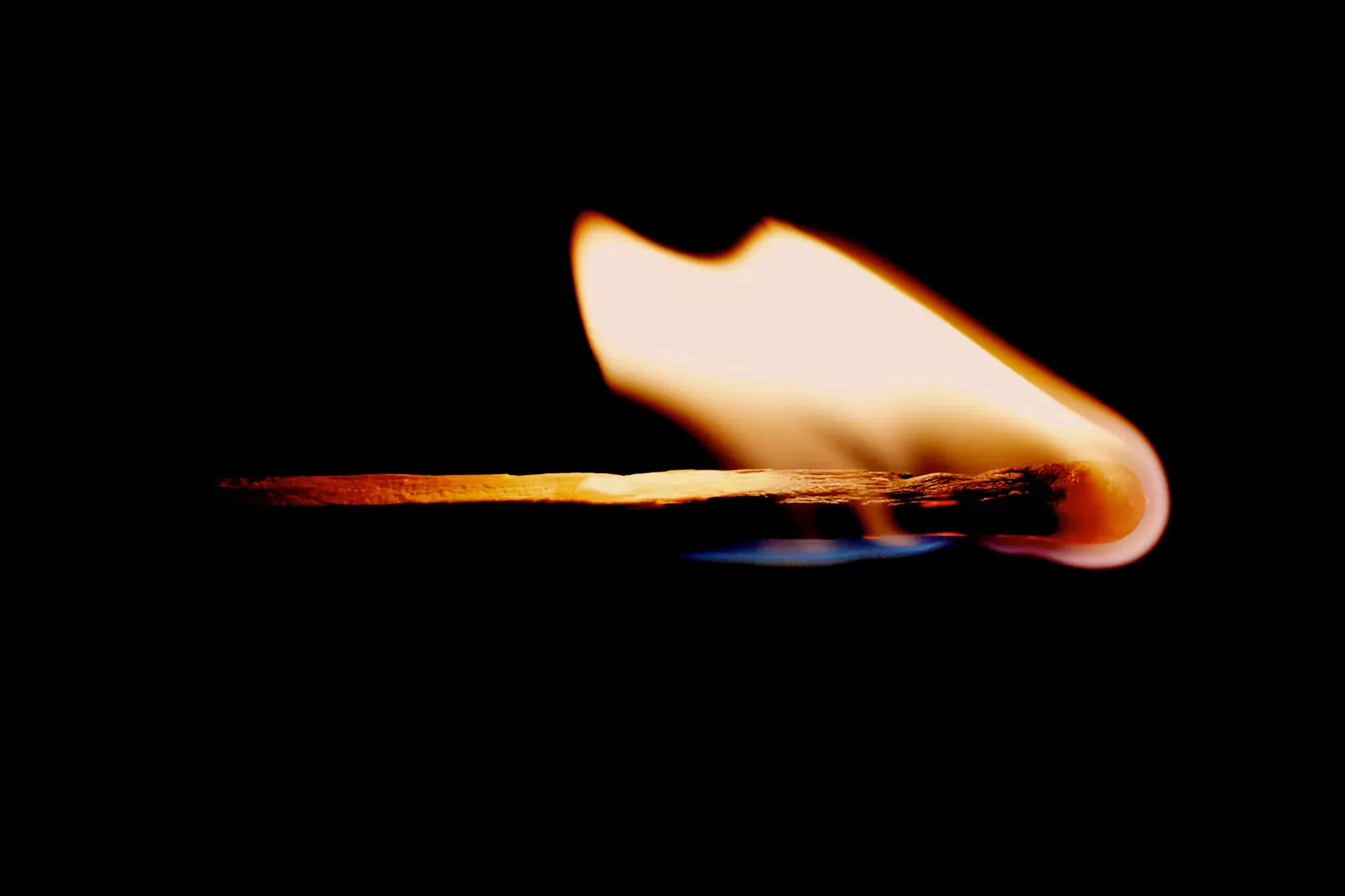 A burning matchstick lying sideways against a black background, its flame curling up from the head, a picture of activation energy in chemical kinetics
