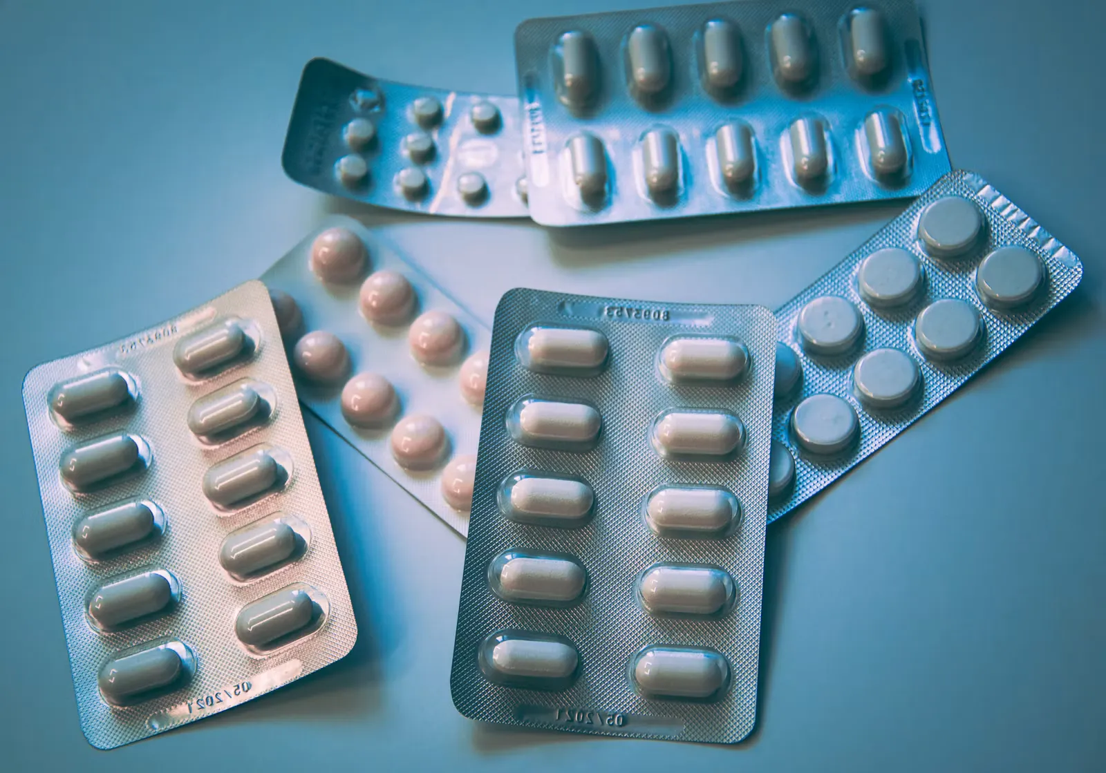 Mehrere aufgefächerte Tablettenblister mit weißen und rosa Tabletten auf blauem Untergrund