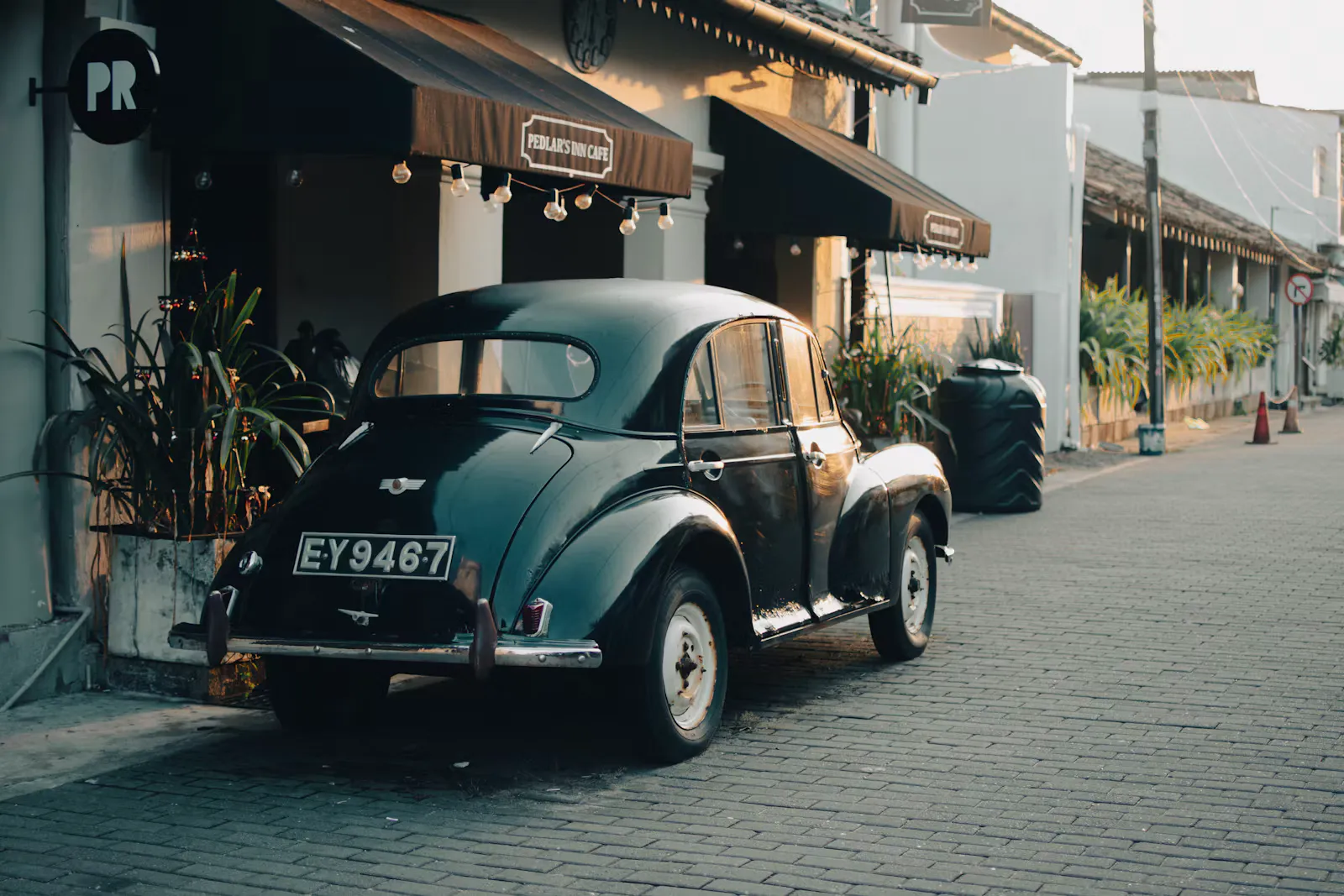 Schwarzer Oldtimer parkt auf einer gepflasterten Straße vor einem Café mit Lichterketten, Abendlicht in der Altstadt von Galle