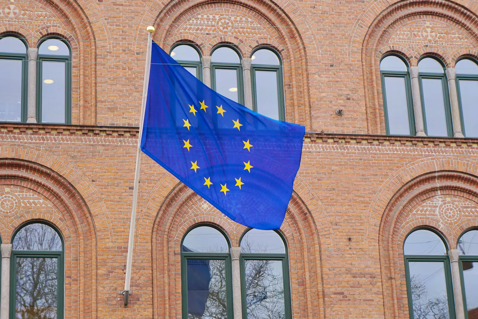 A European Union flag flying in front of a brick building, the kind of authority that decides permanent residence applications
