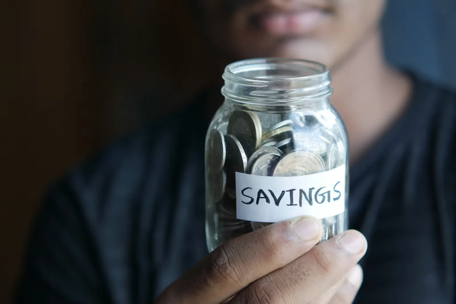 Mann hält ein Sparglas mit der Aufschrift Savings in der Hand