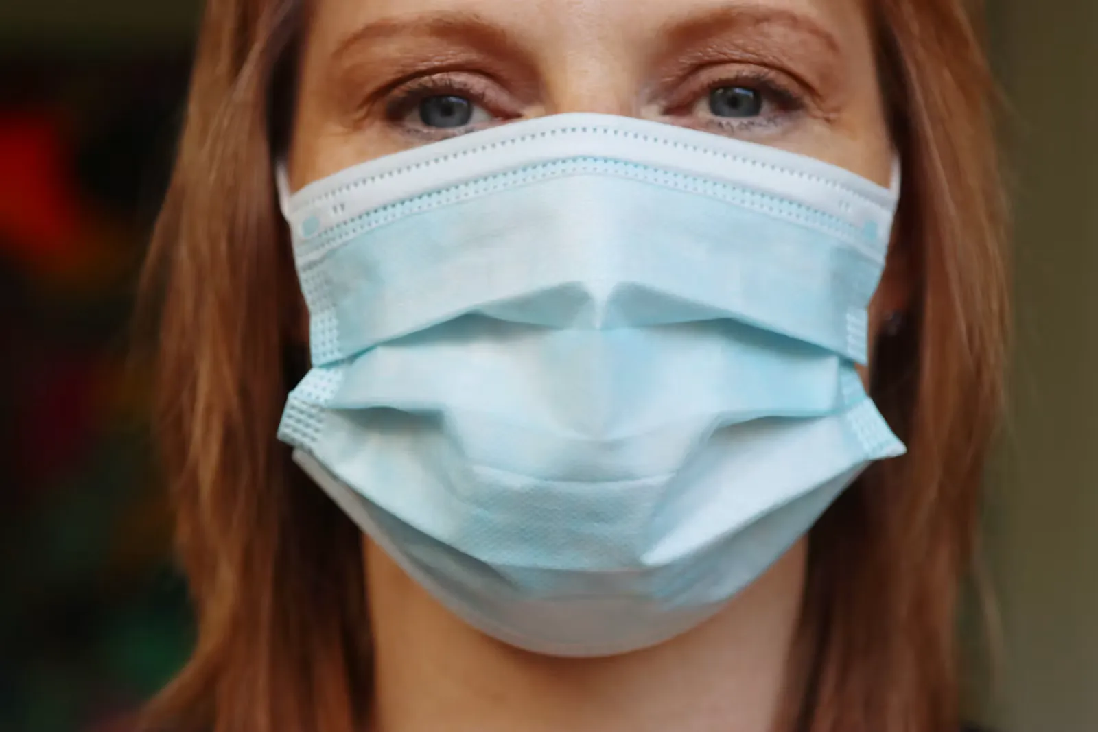 Frau mit hellblauer chirurgischer Gesichtsmaske, nur Augen und Haare sind zu sehen