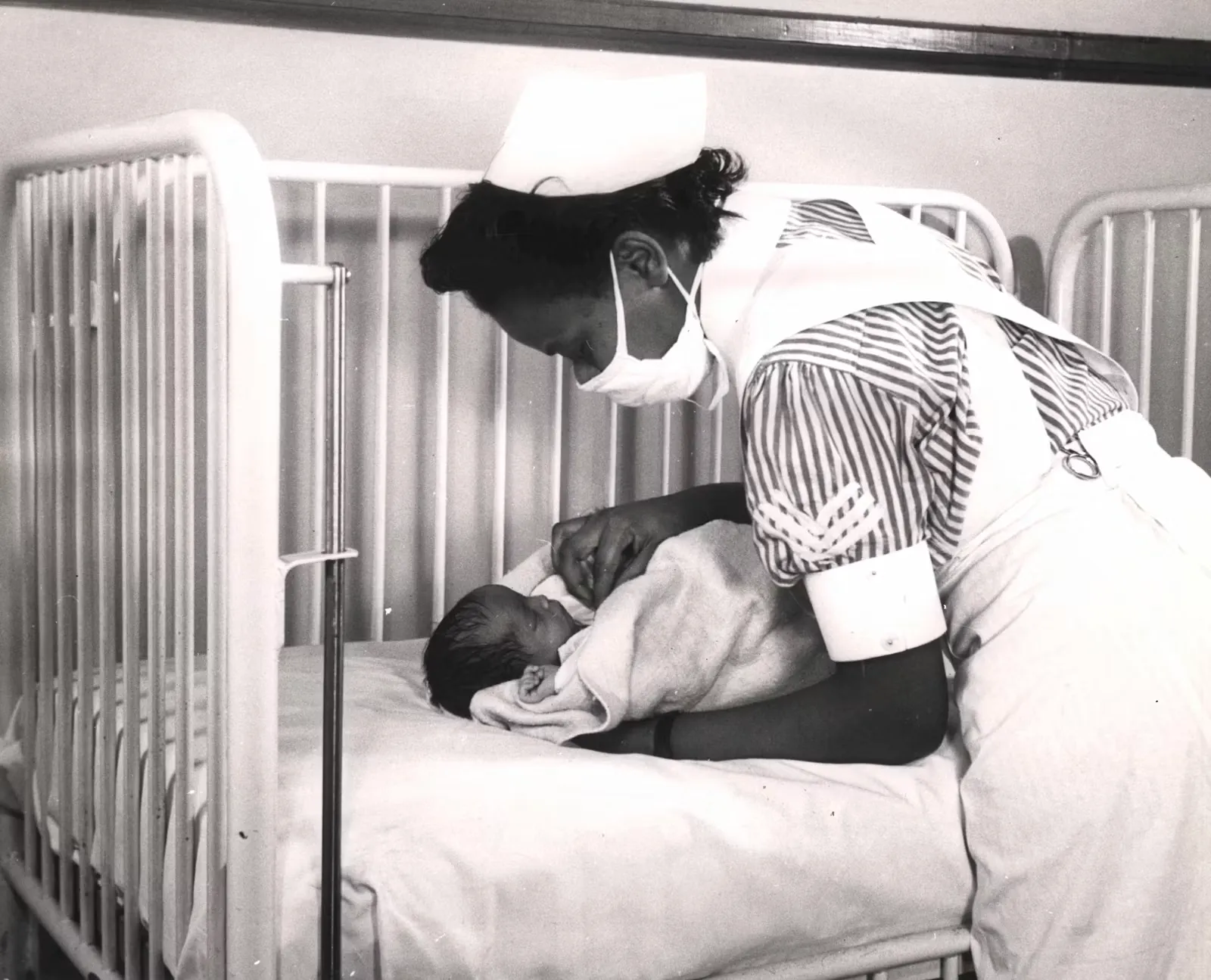 A nurse holding a newborn in a hospital crib