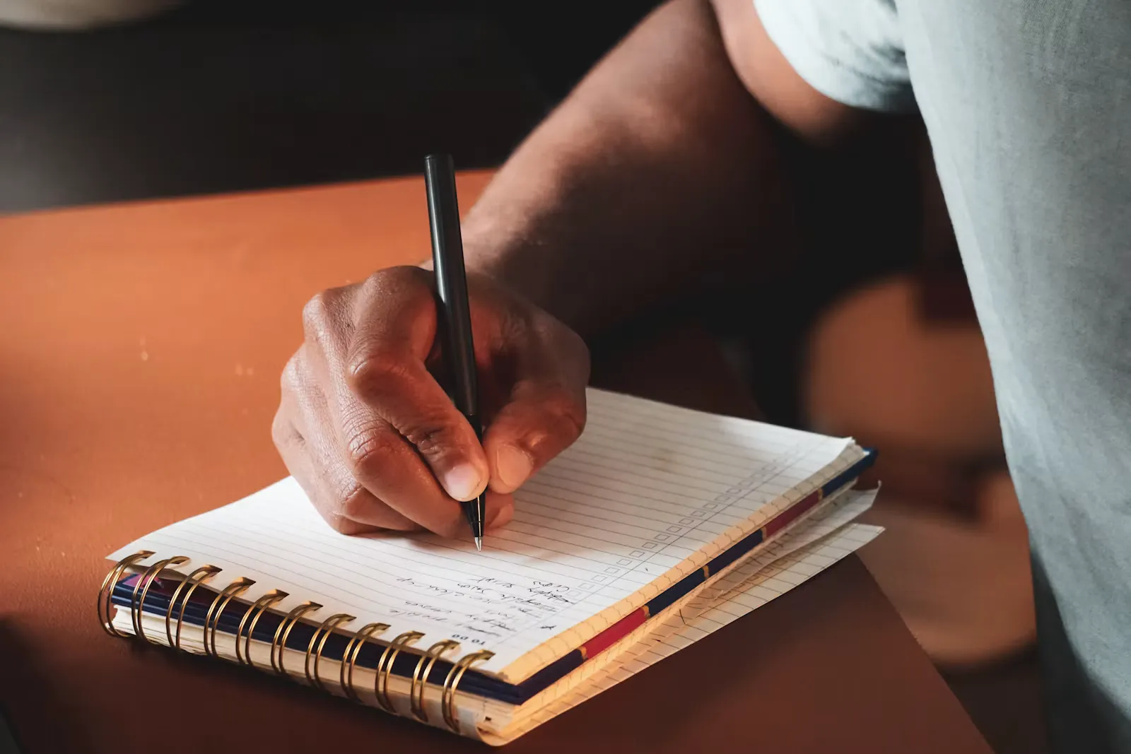A hand writing with a pen on an open notebook page beside a cup, working through practice questions