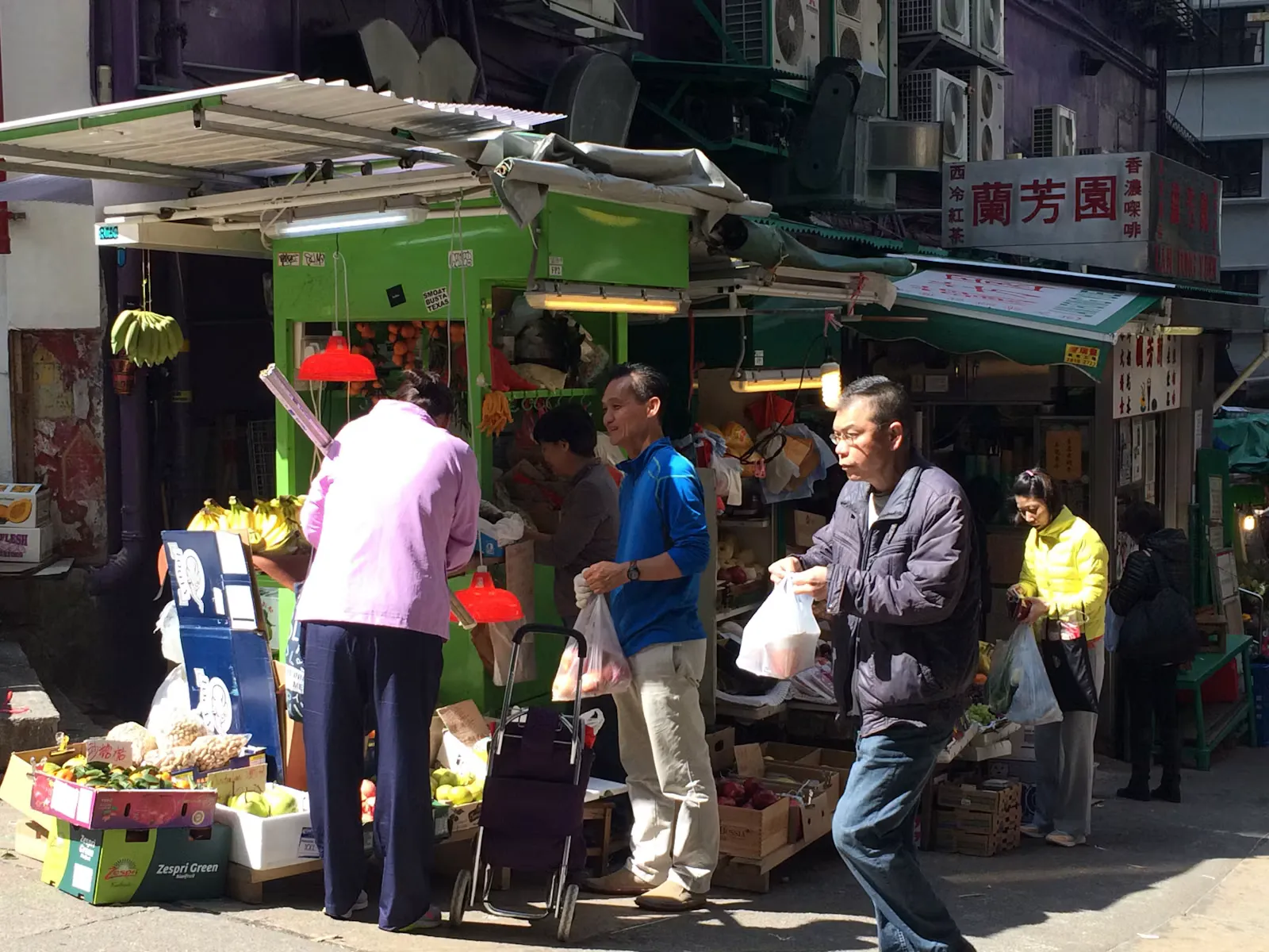 Obst- und Gemüsestand an einer Straßenecke in einer asiatischen Großstadt, Menschen kaufen Bananen und Äpfel, typische Umgebung für Essen und Trinken im Auslandspraktikum