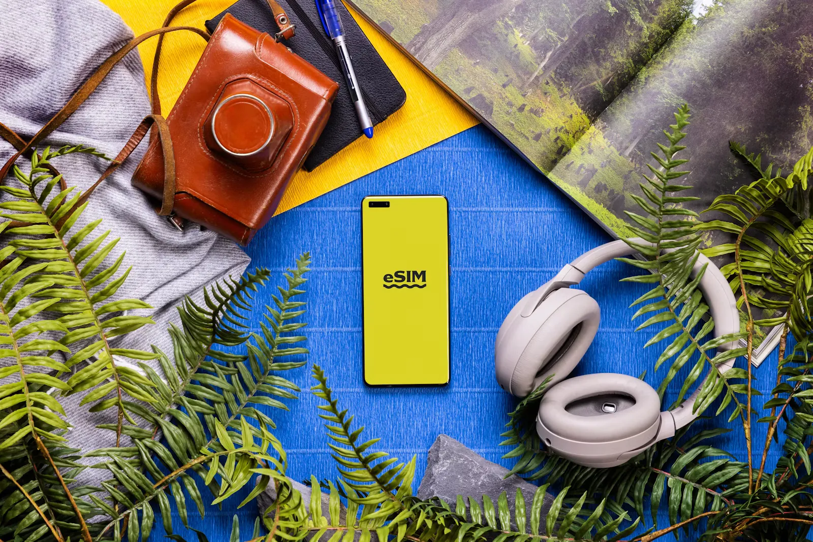 Buch, Kopfhörer, Kamera und ein Smartphone liegen nebeneinander auf einem Tisch – Symbolbild für die Reisevorbereitung mit eSIM vor Famulatur und KPJ