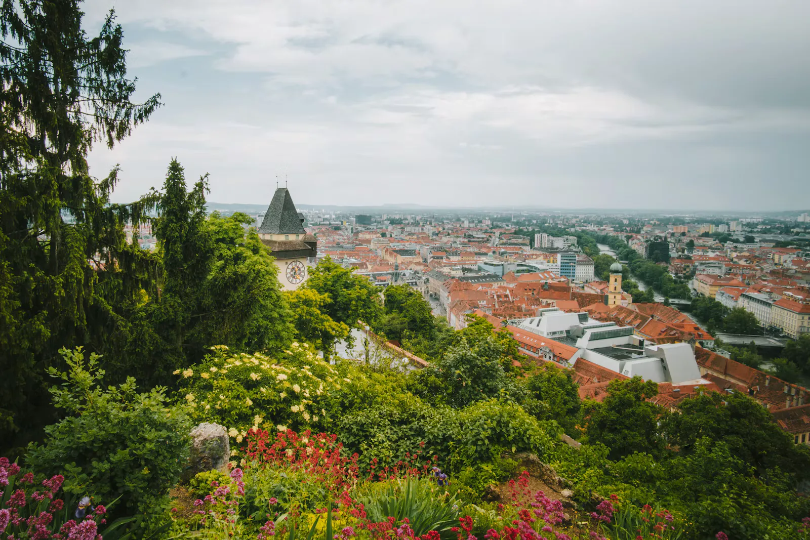 Blick vom Grazer Schlossberg über blühende Beete und den Uhrturm auf die roten Dächer der Altstadt, Symbolbild für die Famulaturplanung an der MedUni Graz
