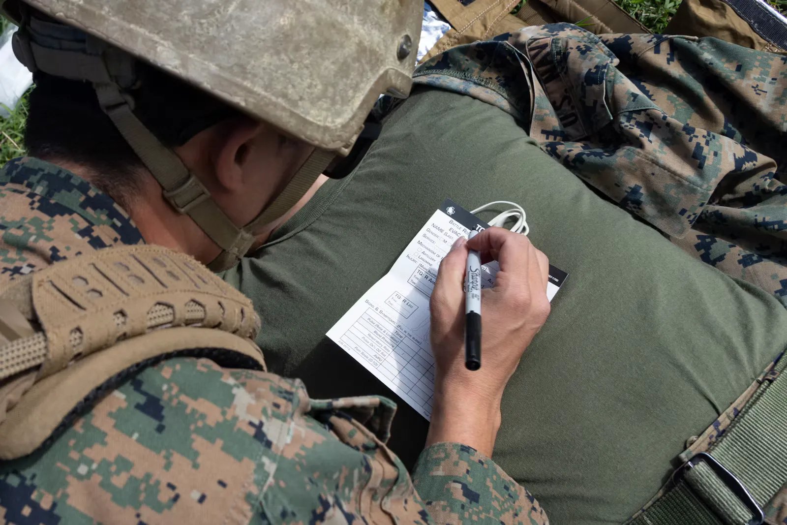 Soldat mit Helm schreibt mit einem Kugelschreiber Notizen auf ein Blatt, das auf einem Rucksack liegt, Sinnbild für Dienstzeit-Bescheinigung und Unterlagen für die Bewerbung