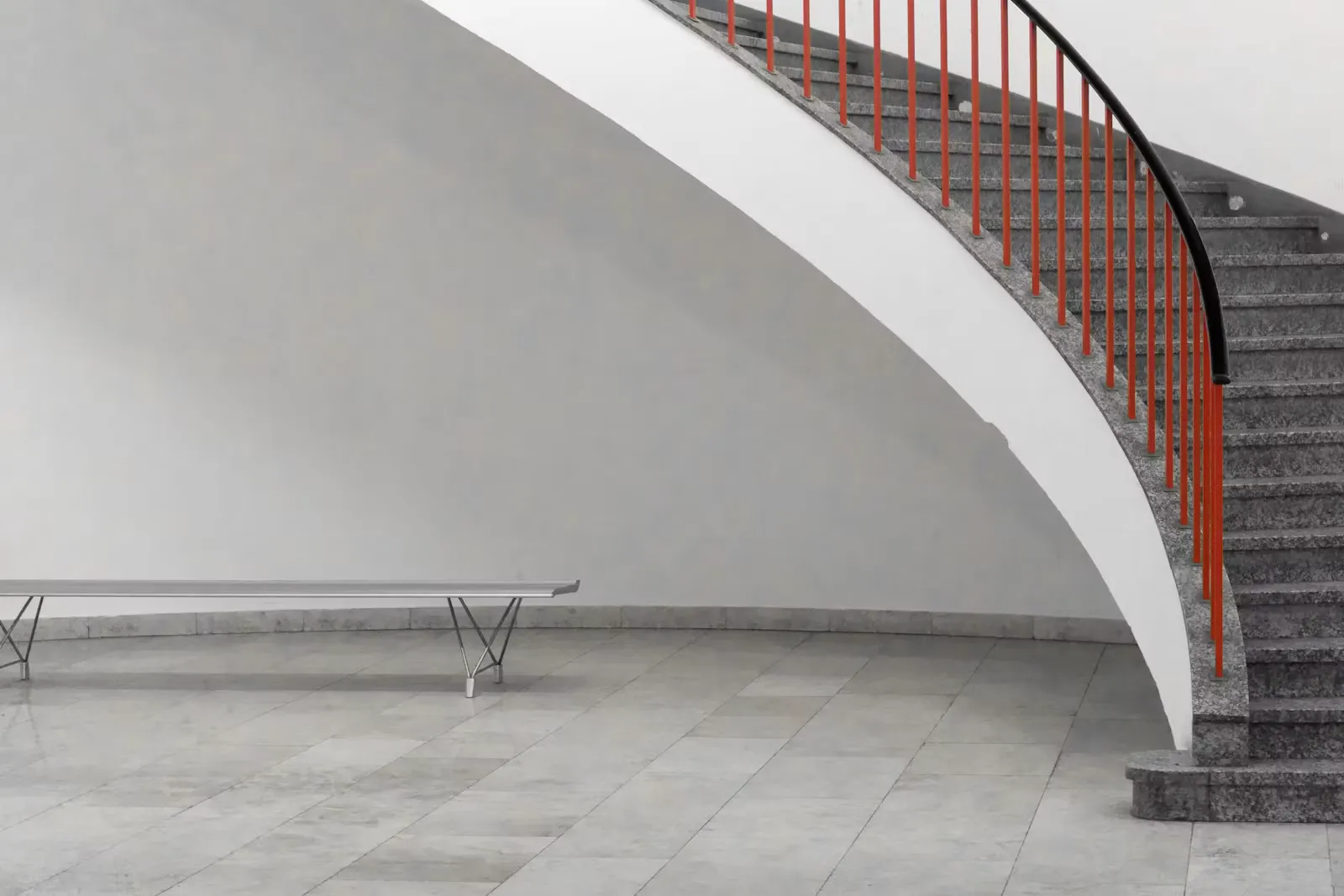Graue Stahlbank unter einer Betontreppe in einem hellen, leeren Universitätsgebäude