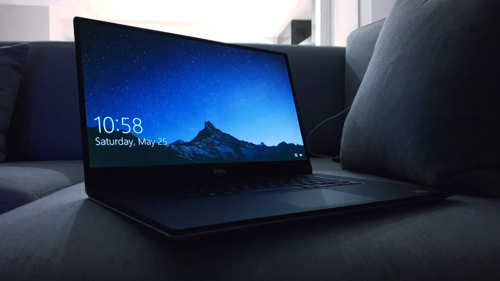 Aufgeklappter schwarzer Laptop auf einem Sofa, daneben ein Kissen