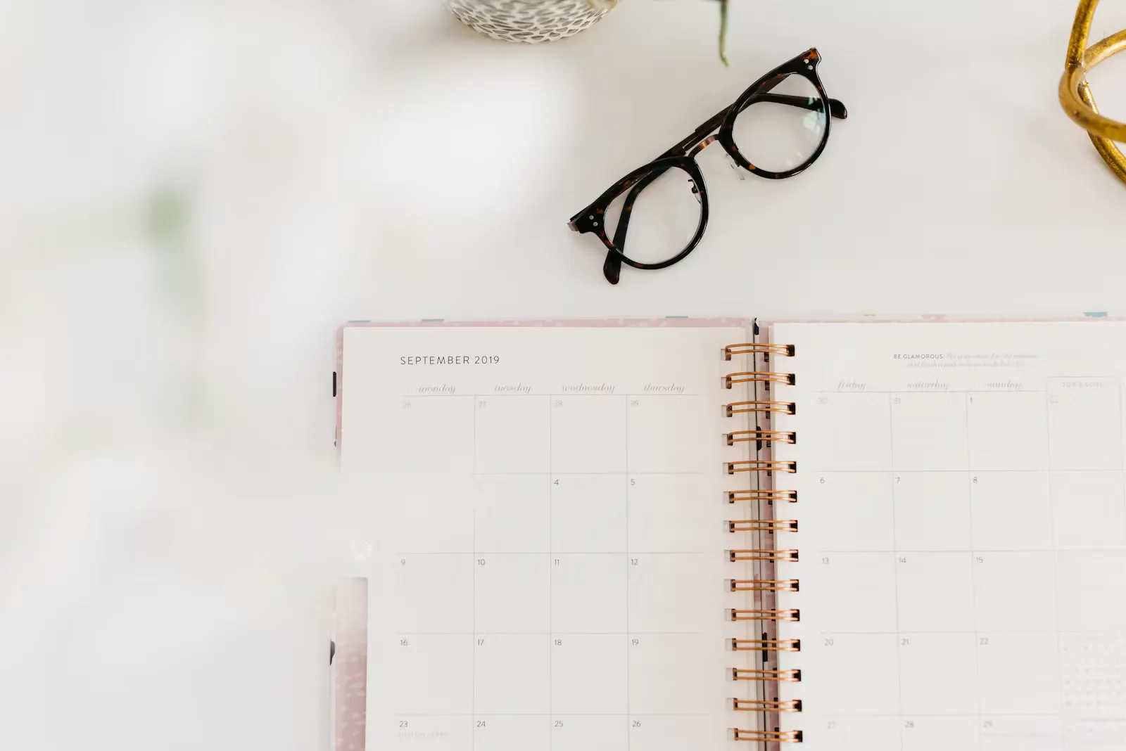 An open spiral monthly planner on a white desk with a pair of black glasses beside it, the kind of page where a NEET study timetable gets written out week by week