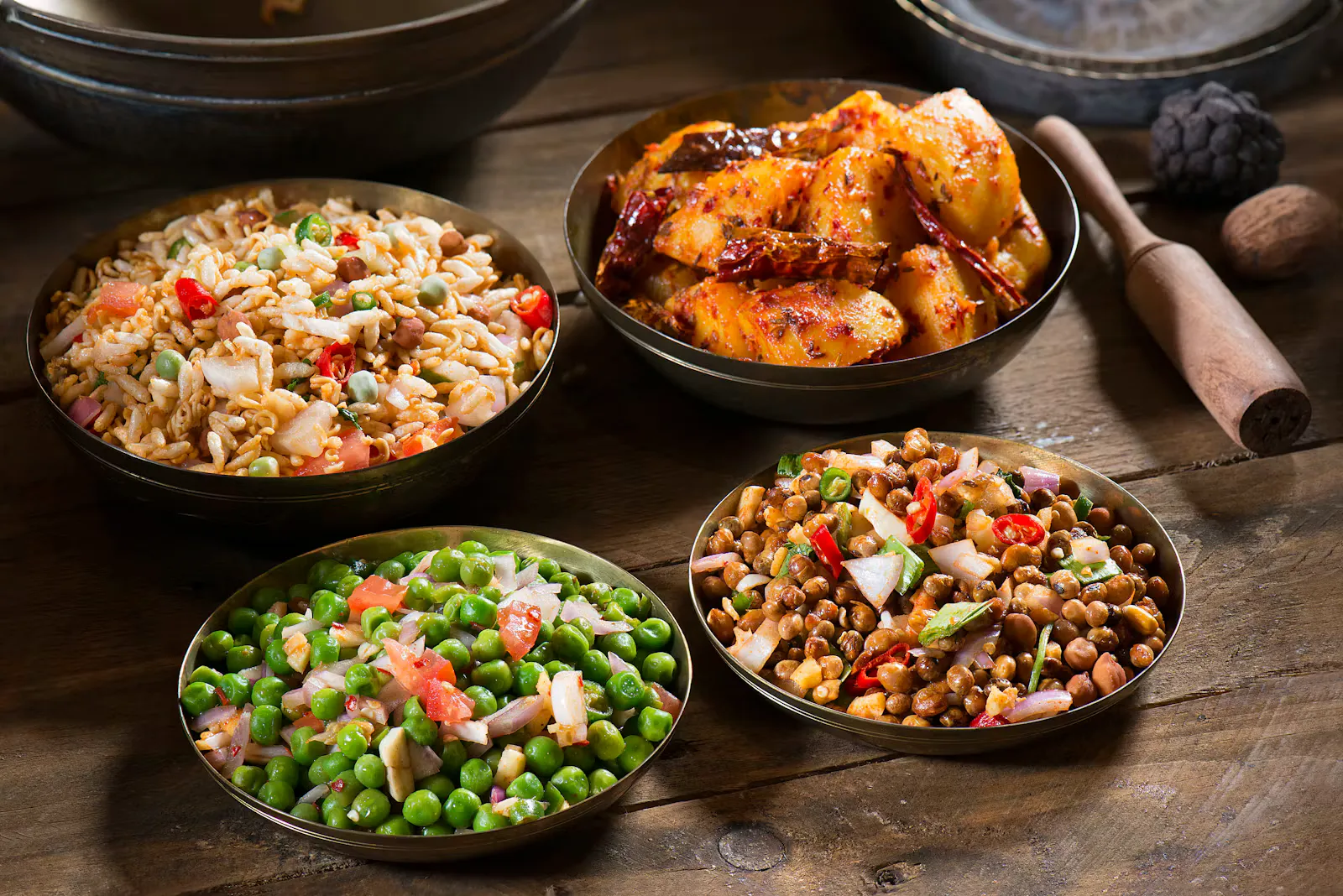 Vier Messingschalen auf einem Holztisch Vier Messingschalen auf einem Holztisch: gewürzte Erdäpfel mit getrockneten Chilischoten, eine Puffreis-Mischung, ein Erbsensalat mit Paradeisern und Zwiebeln sowie ein Salat aus schwarzen Kichererbsen