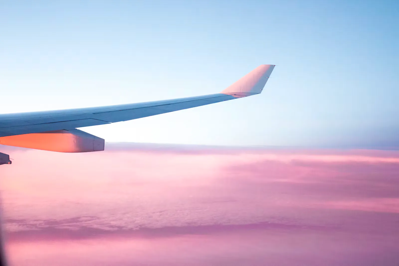 Flugzeugflügel über einem rosa gefärbten Wolkenmeer in der Dämmerung, Symbolbild für den Langstreckenflug ins Praktikum und das Risiko einer Reisethrombose