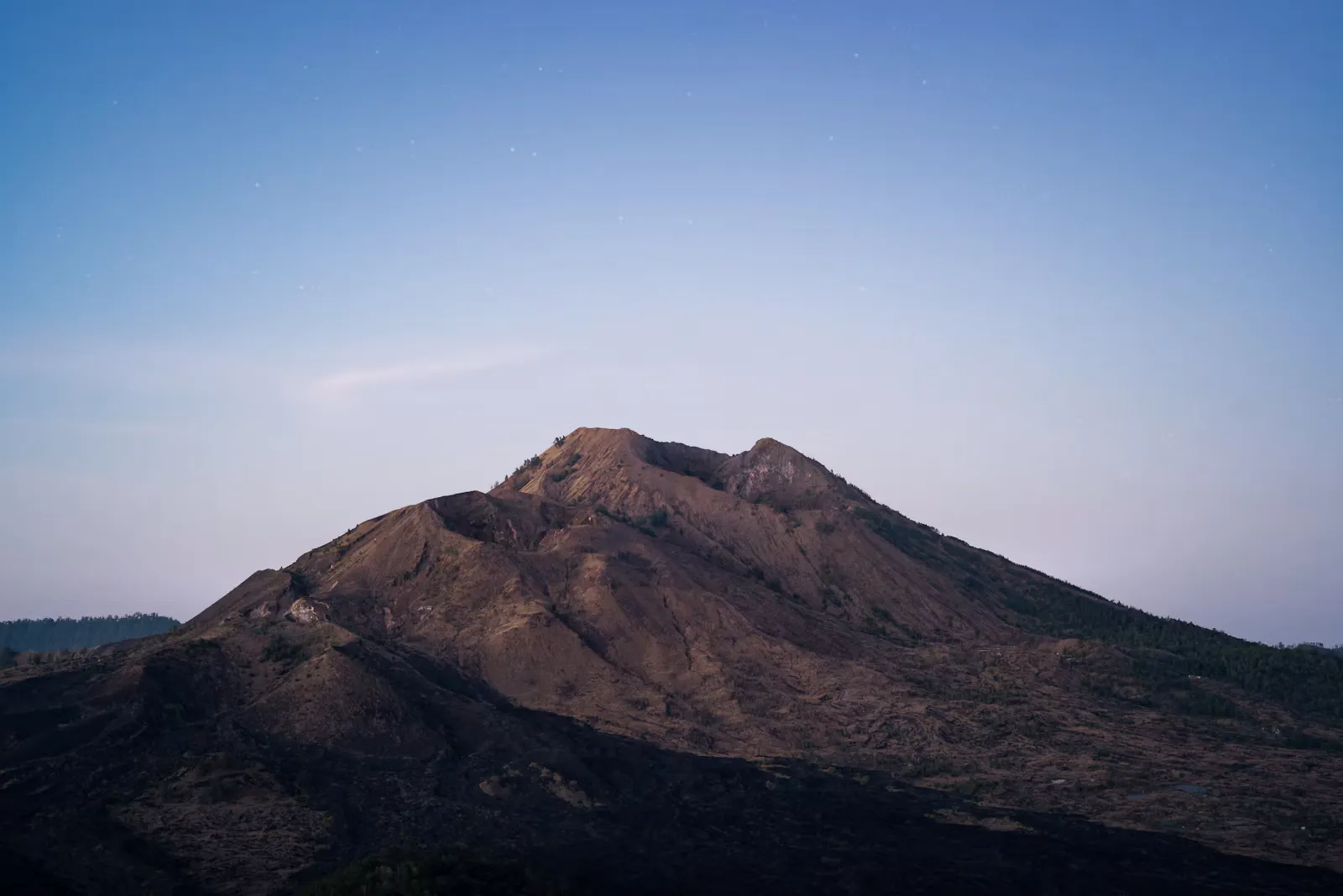 A bare volcanic peak under a clear evening sky with the first stars showing