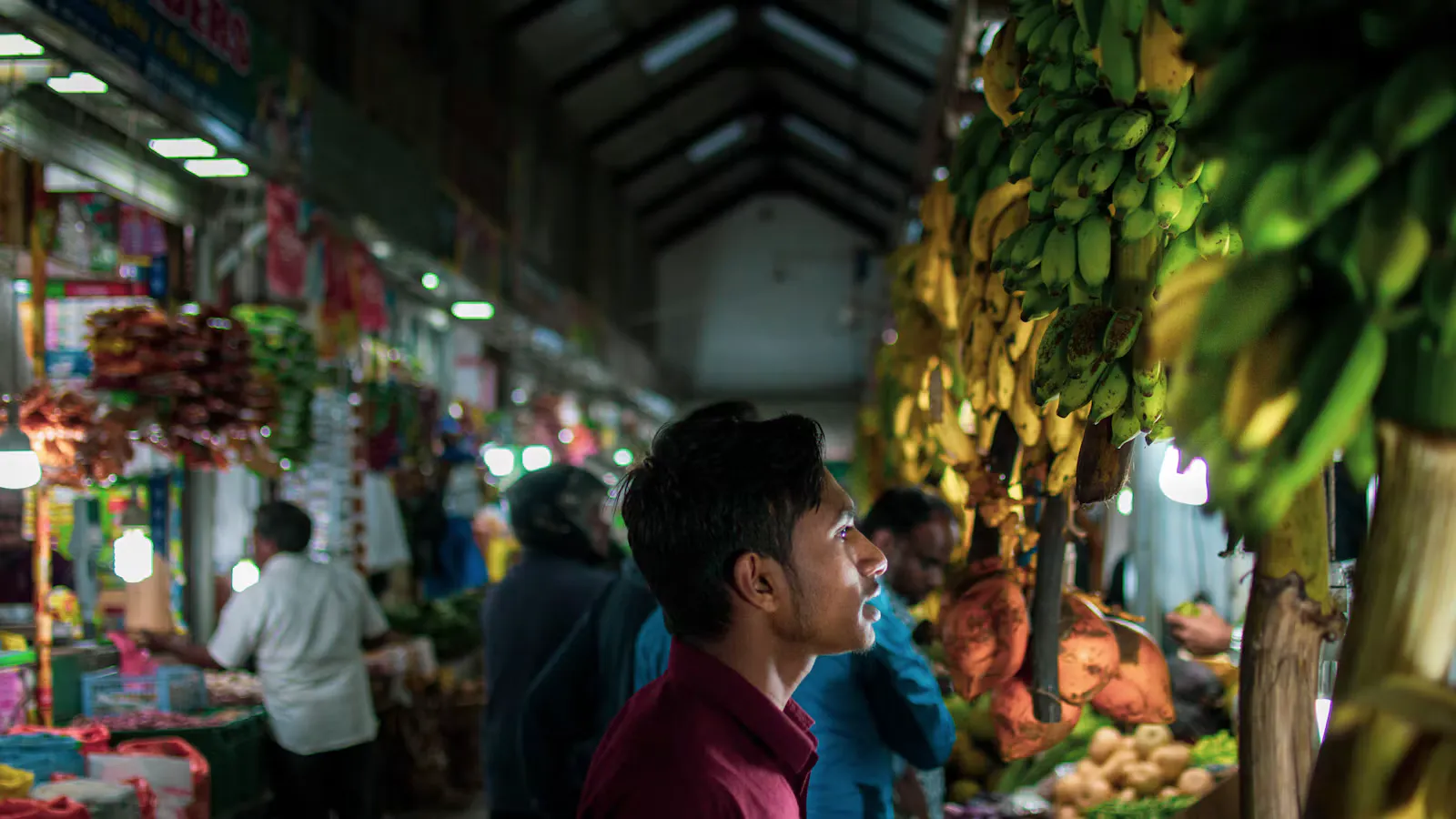 A young man looks at bunches of bananas in a busy indoor market hall in Sri Lanka