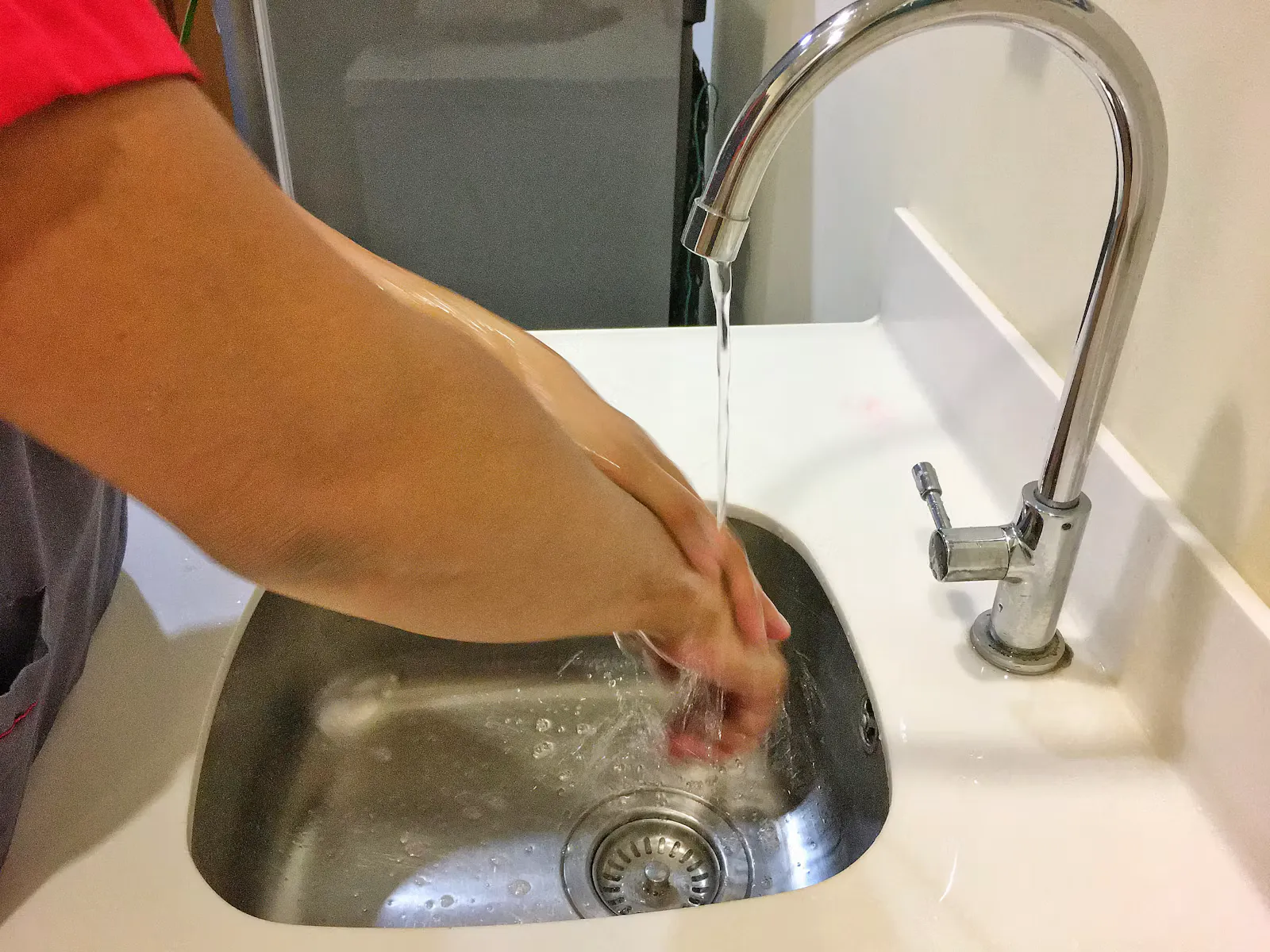 Person wäscht sich die Hände unter einem gebogenen Wasserhahn über einem Spülbecken aus Edelstahl, Händehygiene ergänzt die Polio-Impfung im Praktikum