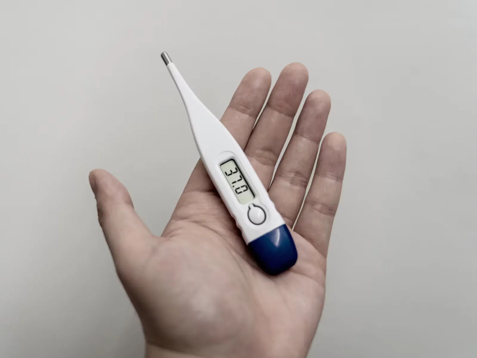 Digitales Fieberthermometer mit blauer Kappe liegt in einer offenen Hand vor hellem Hintergrund