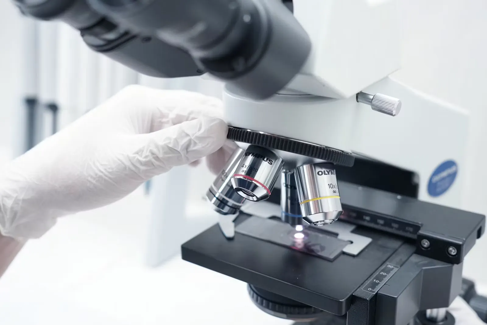 Gloved hand adjusting a glass slide on the stage of a laboratory microscope under bright light