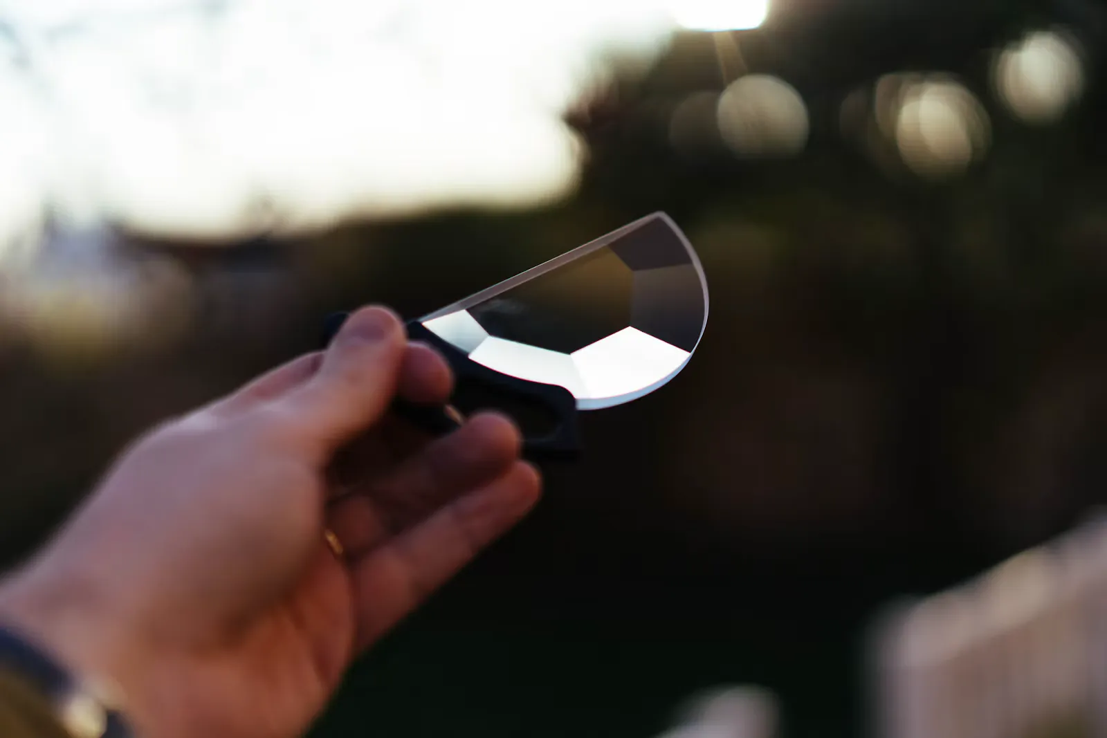 A hand holding a glass prism outdoors that splits sunlight into colours, a reminder that light carries energy in packets in modern physics for NEET