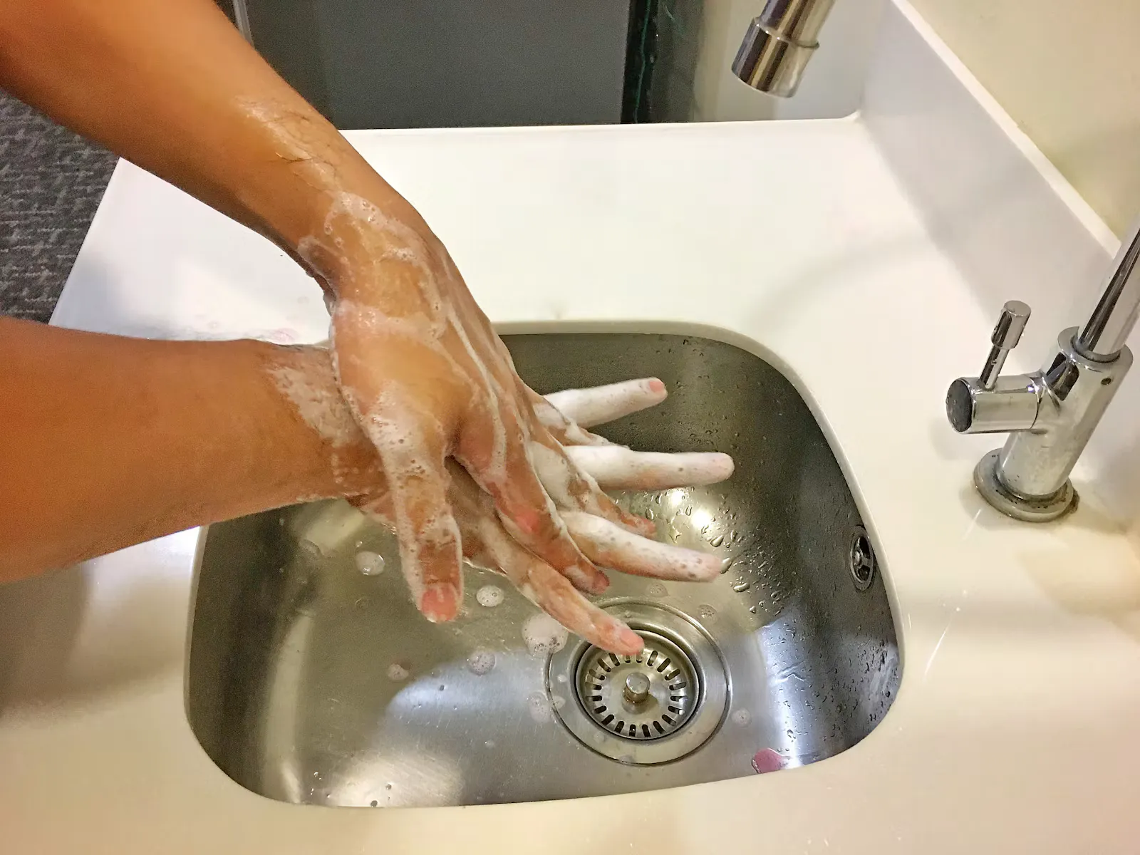 Zwei eingeseifte Hände werden über einem Edelstahlbecken gewaschen, Symbolbild für Handhygiene gegen Polio im Auslandspraktikum