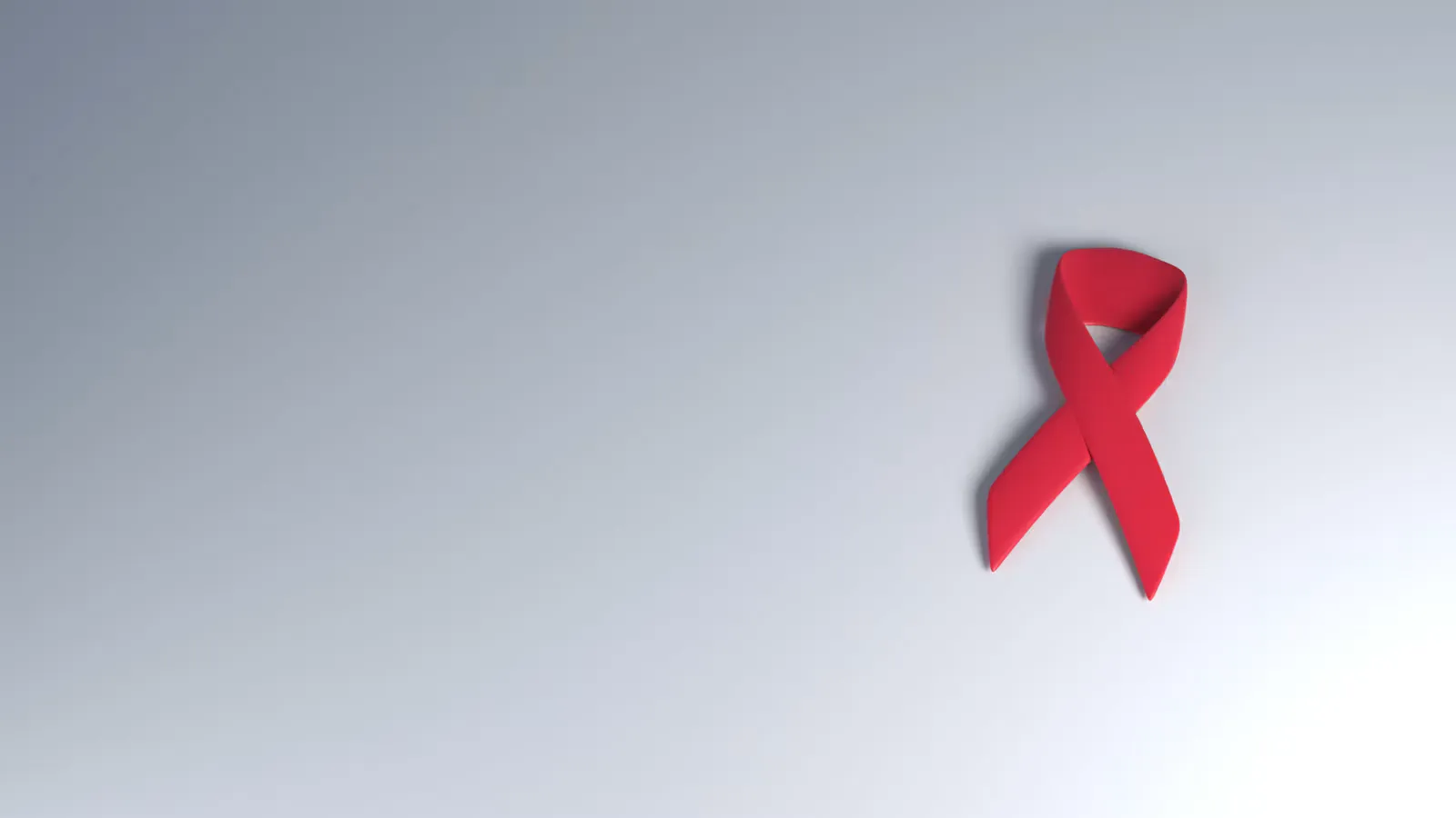 A single red awareness ribbon lying on a plain grey and white surface