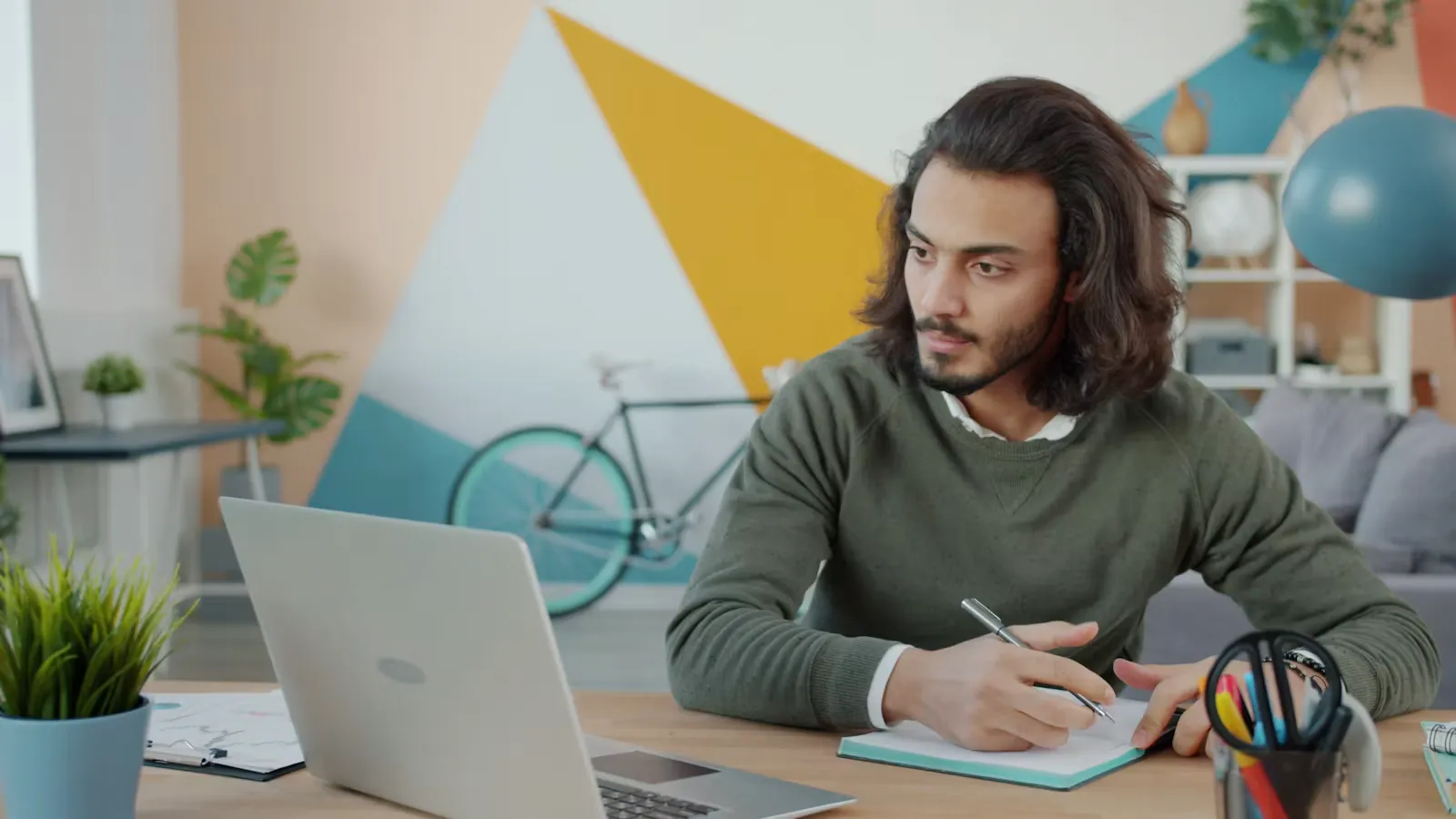 Person sitzt an einem Schreibtisch mit Laptop und Notizblock und plant Unterlagen für das Auslandssemester