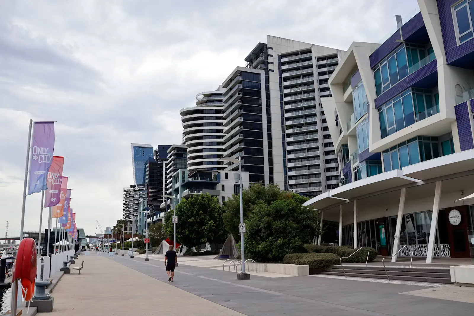 Modern buildings along an Australian waterfront promenade lined with flags