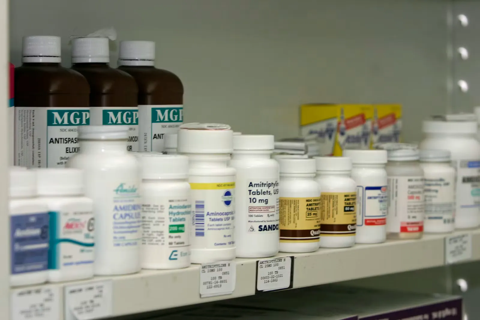 Rows of labelled medicine bottles and tablet boxes lined up along a pharmacy shelf