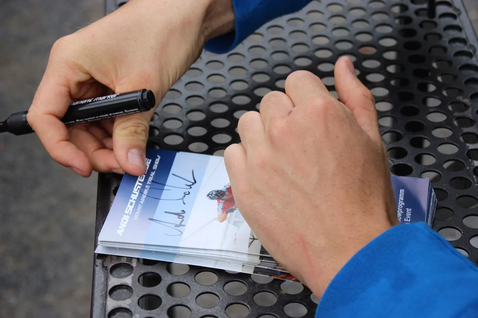 Person hält einen Stift, daneben ein Buch auf dem Tisch
