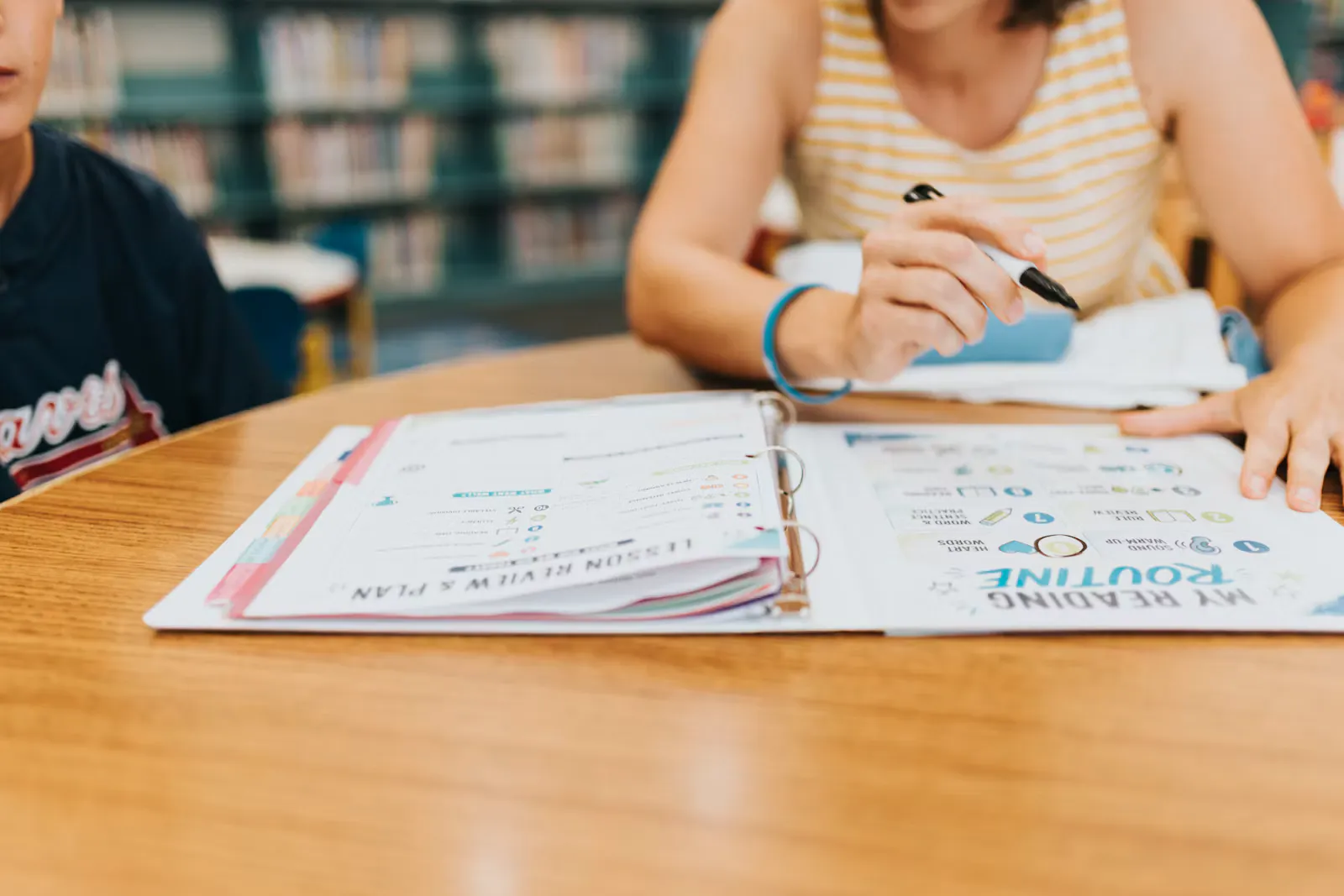 A student marking an open binder of printed study pages with a pen at a wooden library table, the kind of careful check to make before choosing a NEET qualification code