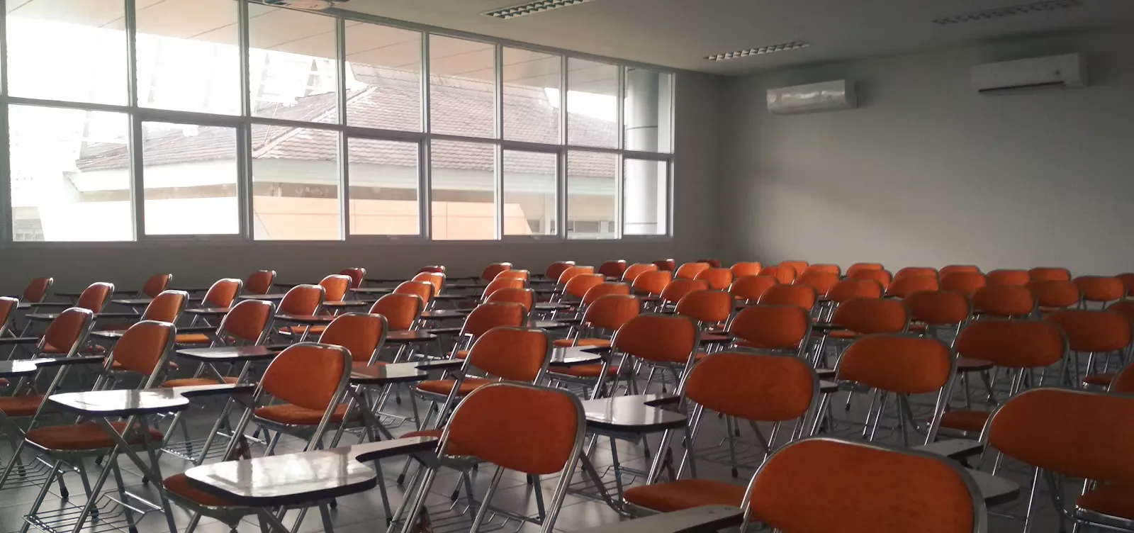 Rows of empty orange chairs with attached writing desks in a bare examination hall