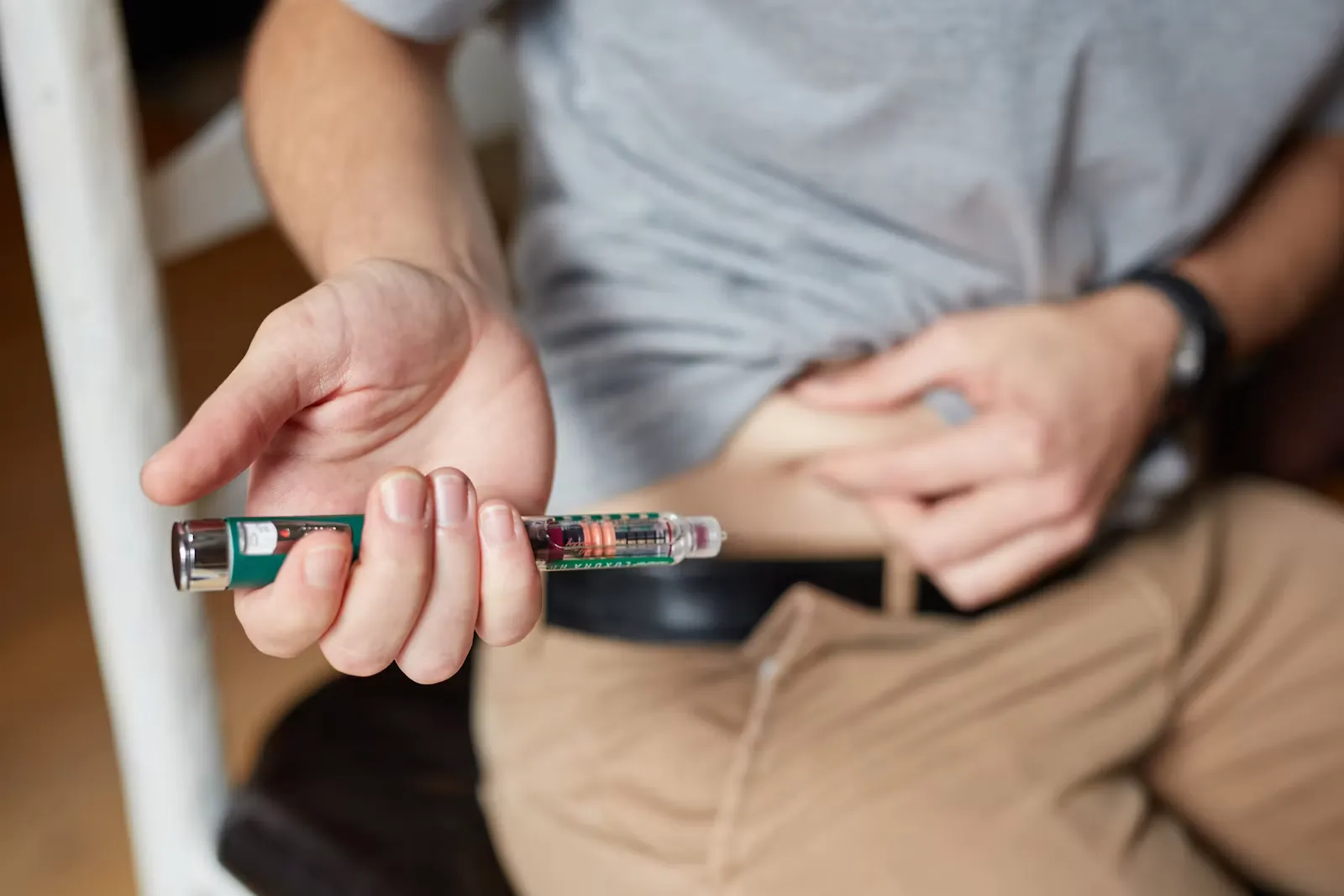 A seated man holding an insulin pen in one hand while pinching a fold of skin on his abdomen with the other